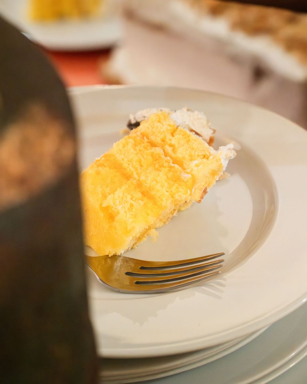 A slice of golden yellow layer cake with white frosting on a white plate with a fork.