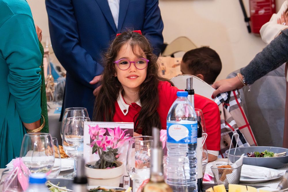 Young girl with red glasses smiling at a festive dining table with water bottles and glassware.