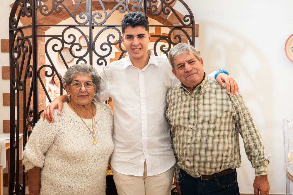 Young man poses with elderly couple in front of decorative iron gate at a family gathering.