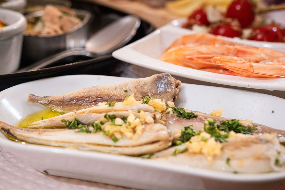 Elegant seafood platter featuring herb-garnished fish fillets with shrimp and cherry tomatoes on white dishes.