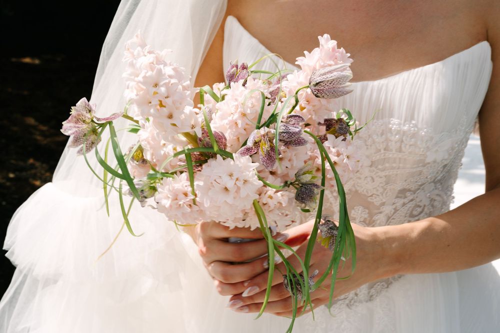 Bride in white strapless gown holding a delicate bouquet of soft pink and lavender wildflowers on her wedding day.