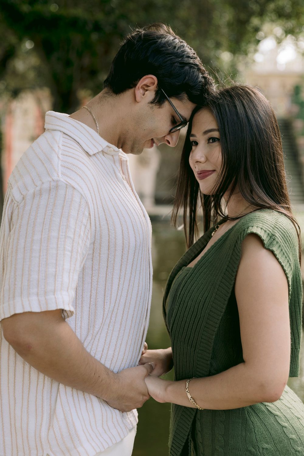 Young couple holding hands and gazing at each other tenderly in an outdoor garden setting.