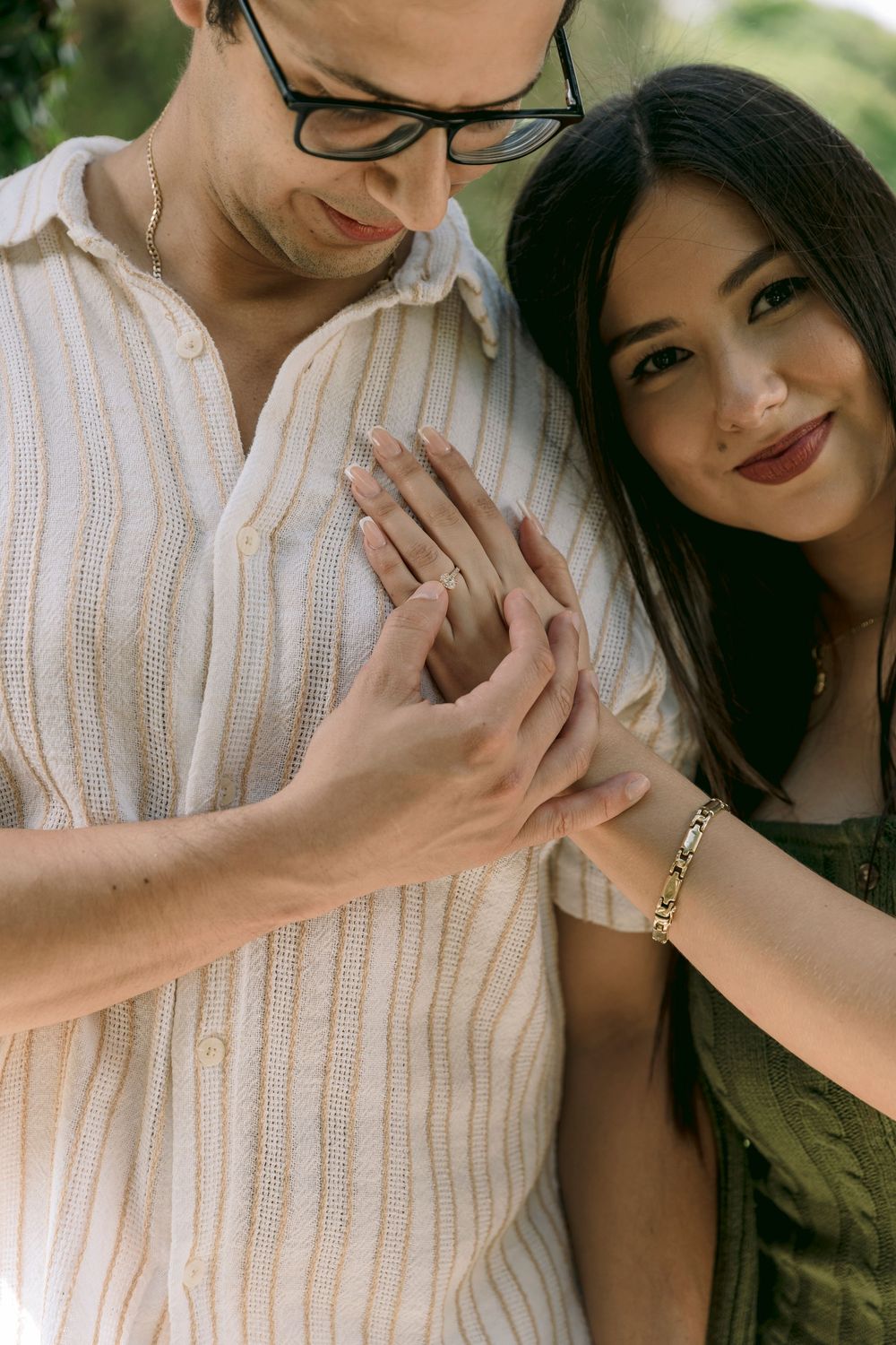 Smiling couple examining engagement ring together, woman in green dress leaning on man.
