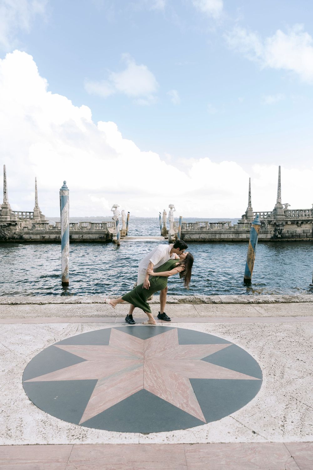 Couple sharing a dip kiss on a decorative compass rose by a scenic waterfront dock.