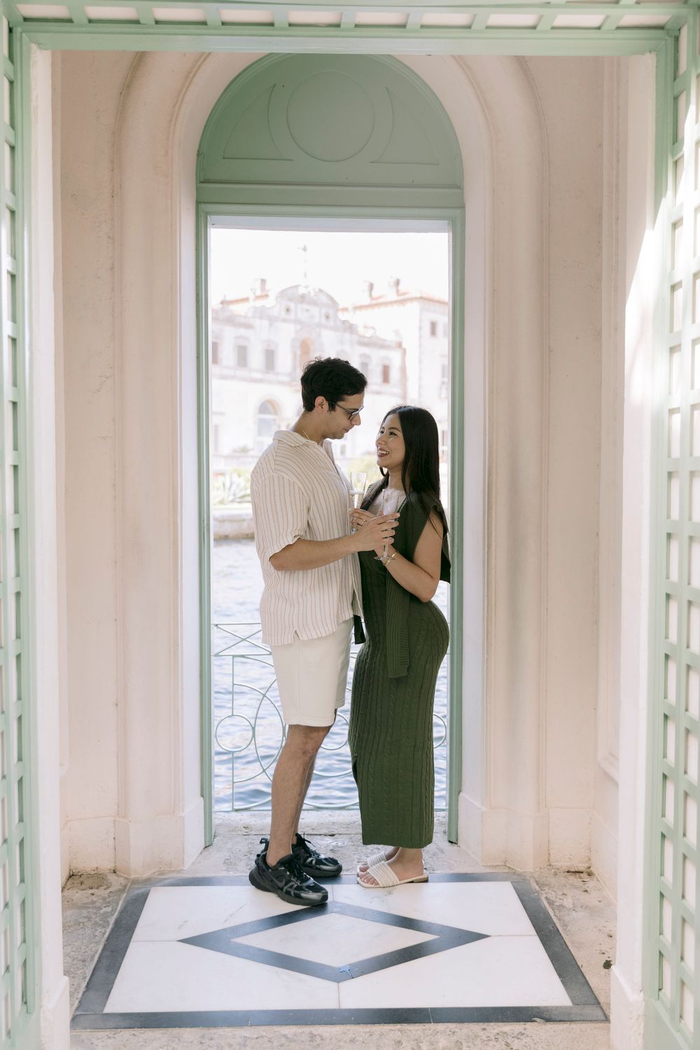 Couple sharing an intimate moment in elegant pastel archway overlooking waterfront.