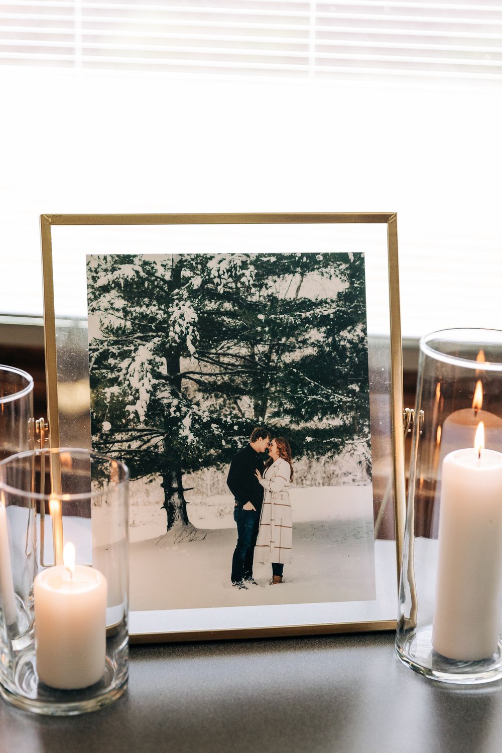 Framed black and white engagement photo of couple in snow displayed between two white pillar candles.