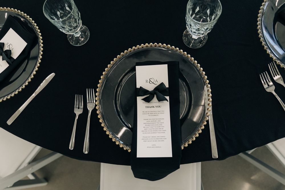 Formal black and gold wedding place setting with menu tied in black ribbon on elegant charger plate.