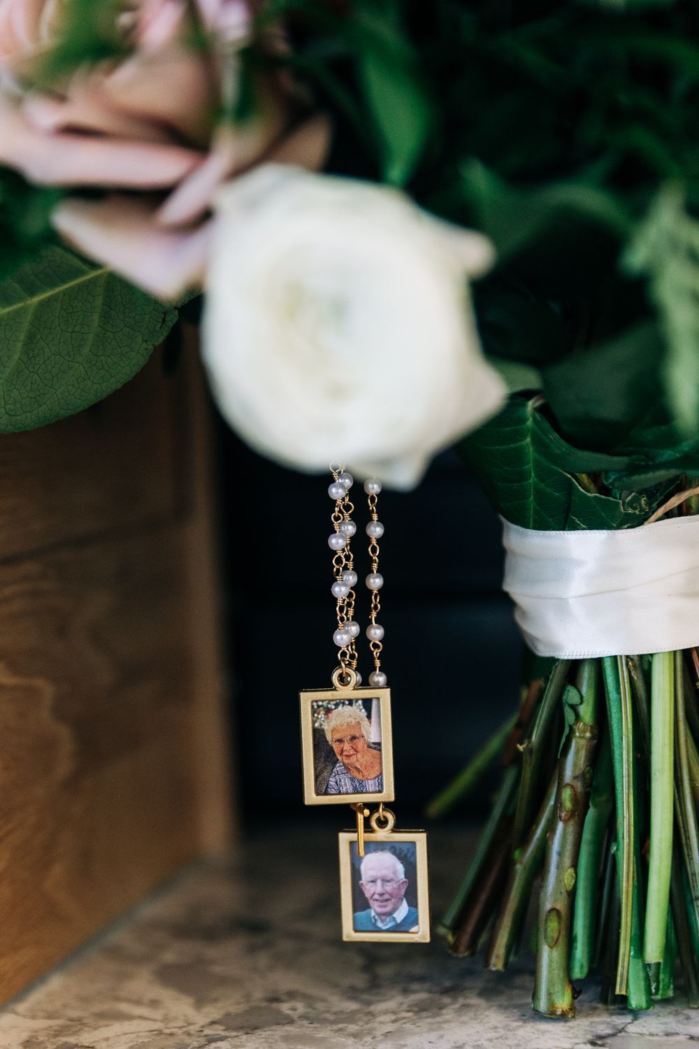 Gold locket bouquet charm with photos of loved ones hanging from a pearl chain on a bridal bouquet.