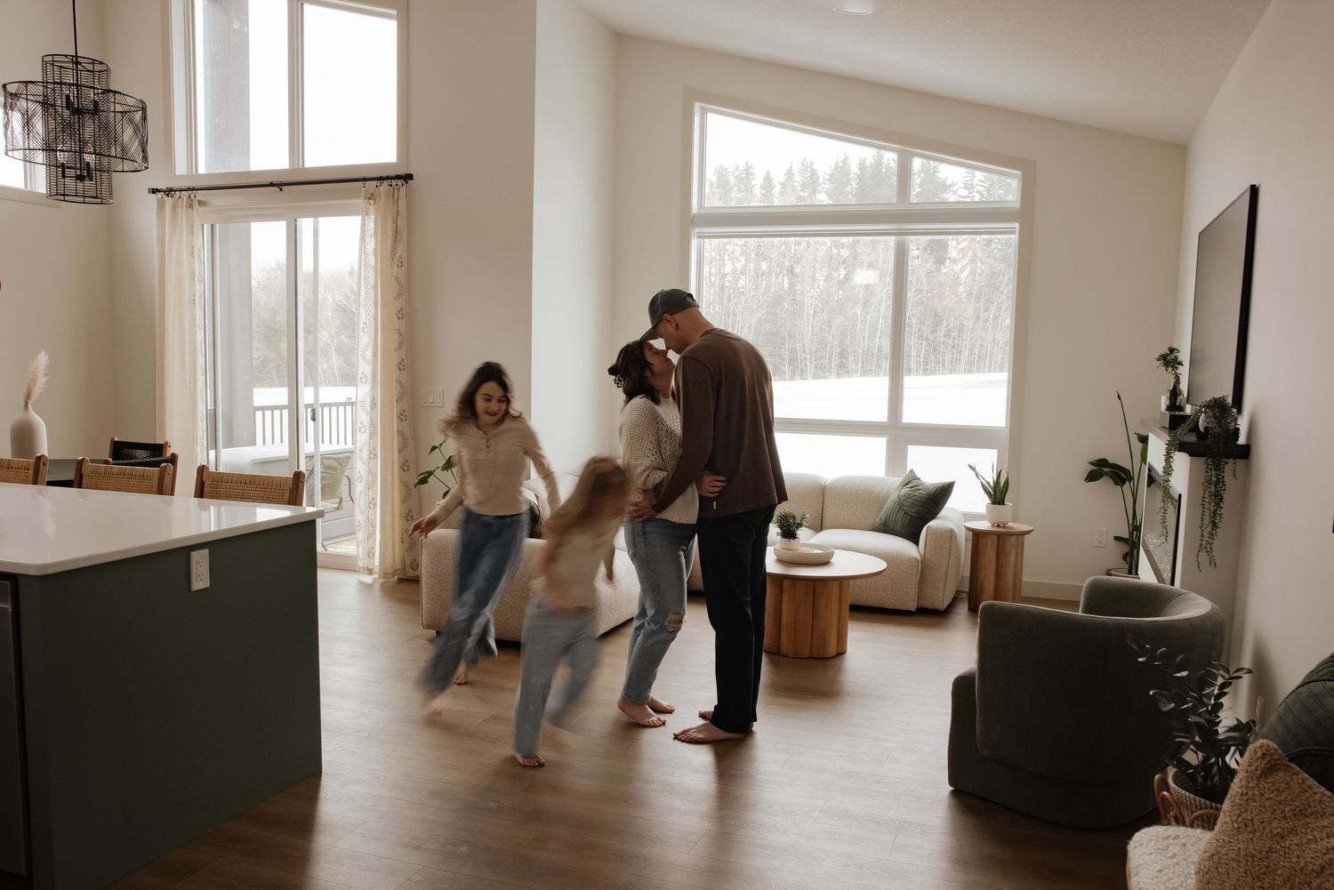 Family enjoying a spacious modern living room with large windows, hardwood floors, and bright natural light.