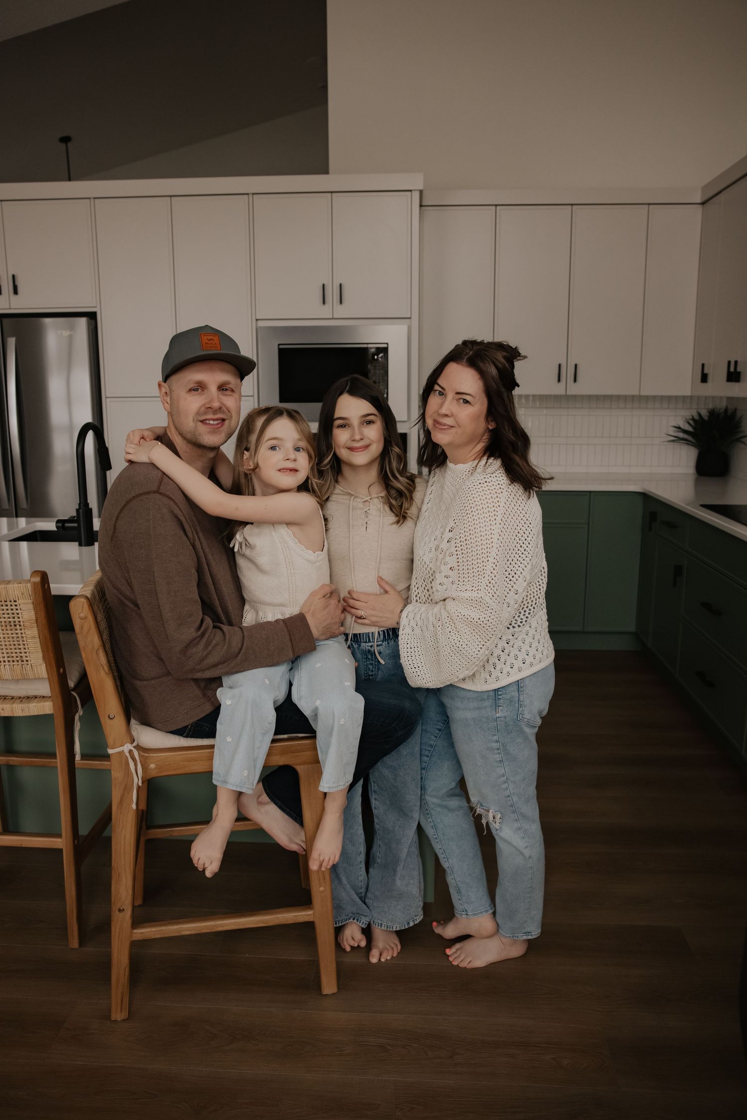 Family of four posing together in a modern kitchen with green cabinets and white countertops.