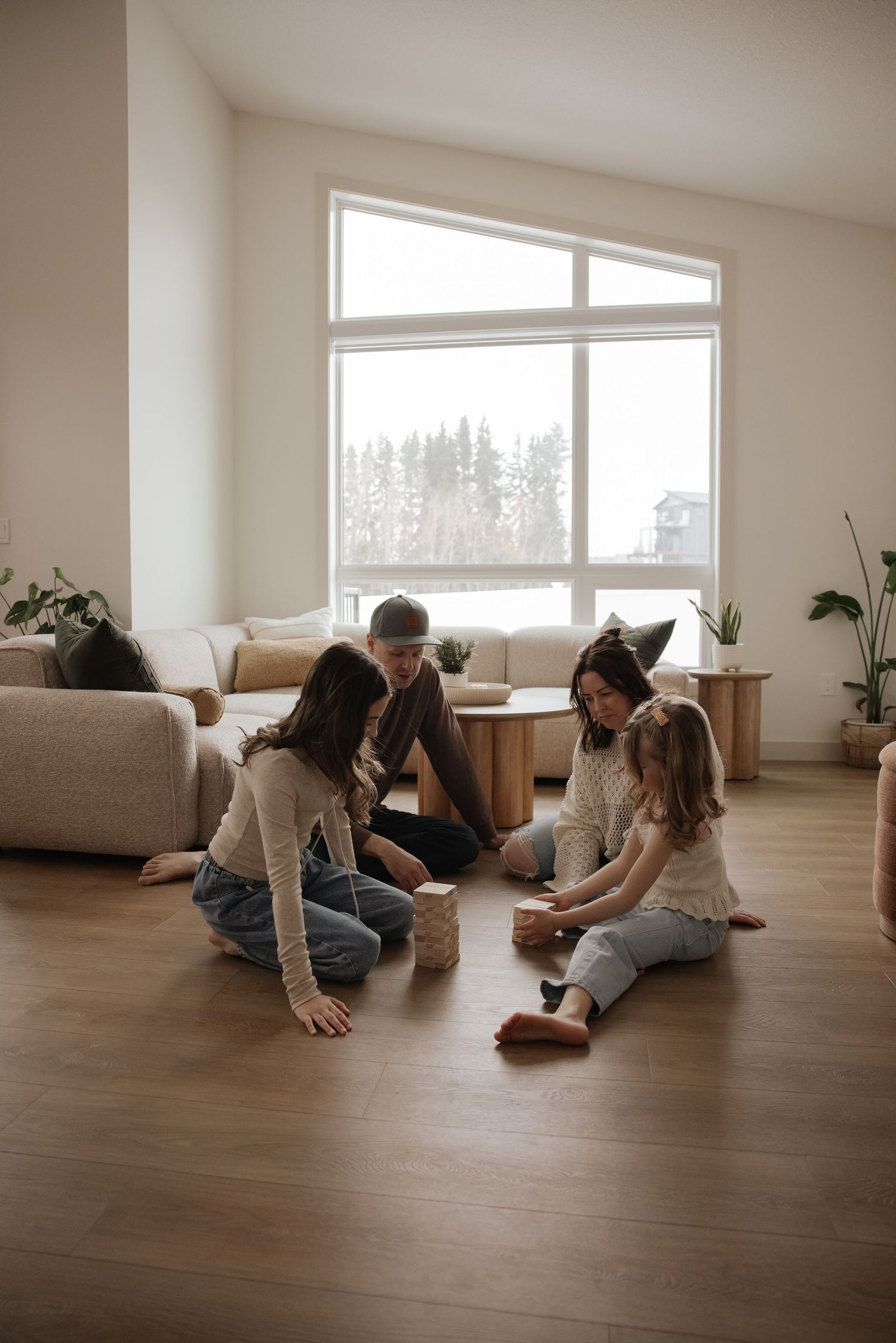 Family of four playing Jenga together on hardwood floor in bright modern living room.