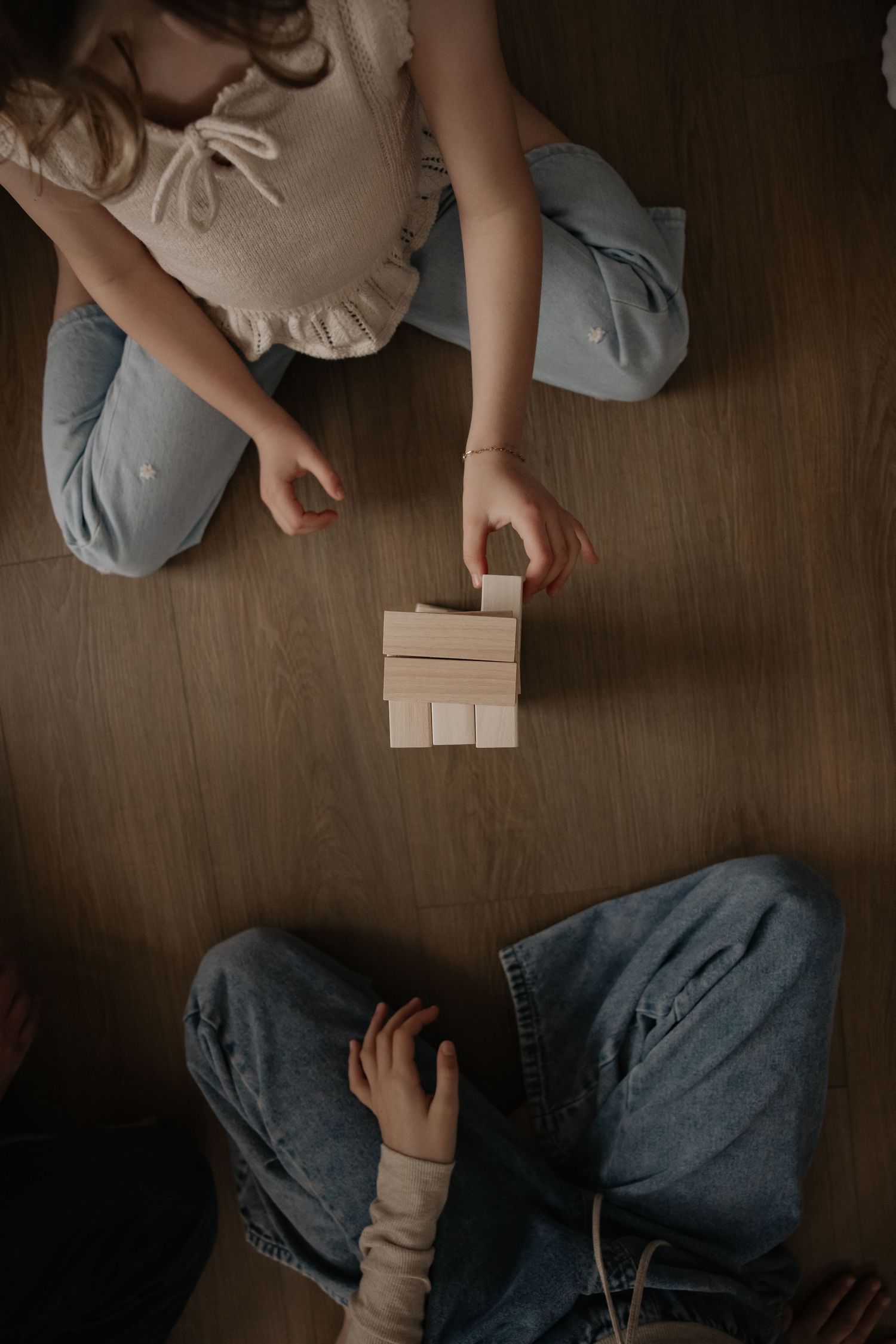 Two children sitting on wood floor playing with wooden building blocks together.