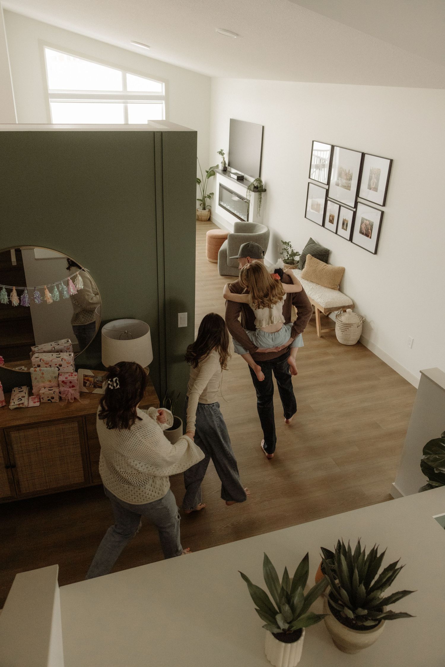 Aerial view of a family walking through a modern home with green accent wall, hardwood floors, and gallery wall decor.