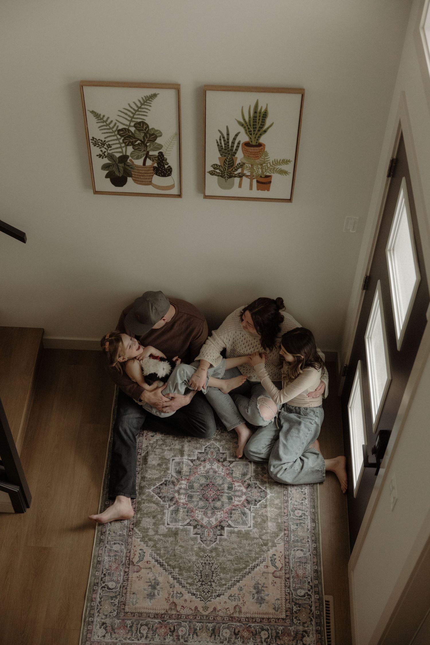 Aerial view of a family sitting together on a vintage rug, surrounded by botanical wall art and natural light.