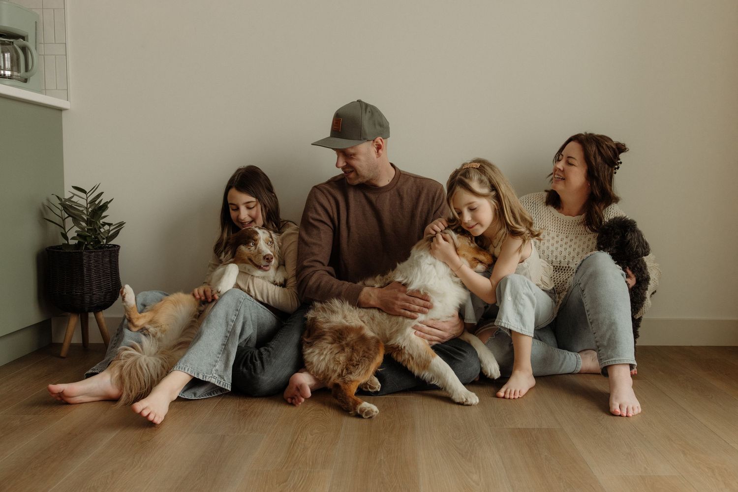 Family of four sitting on floor with two dogs, smiling and bonding together in a bright modern home.