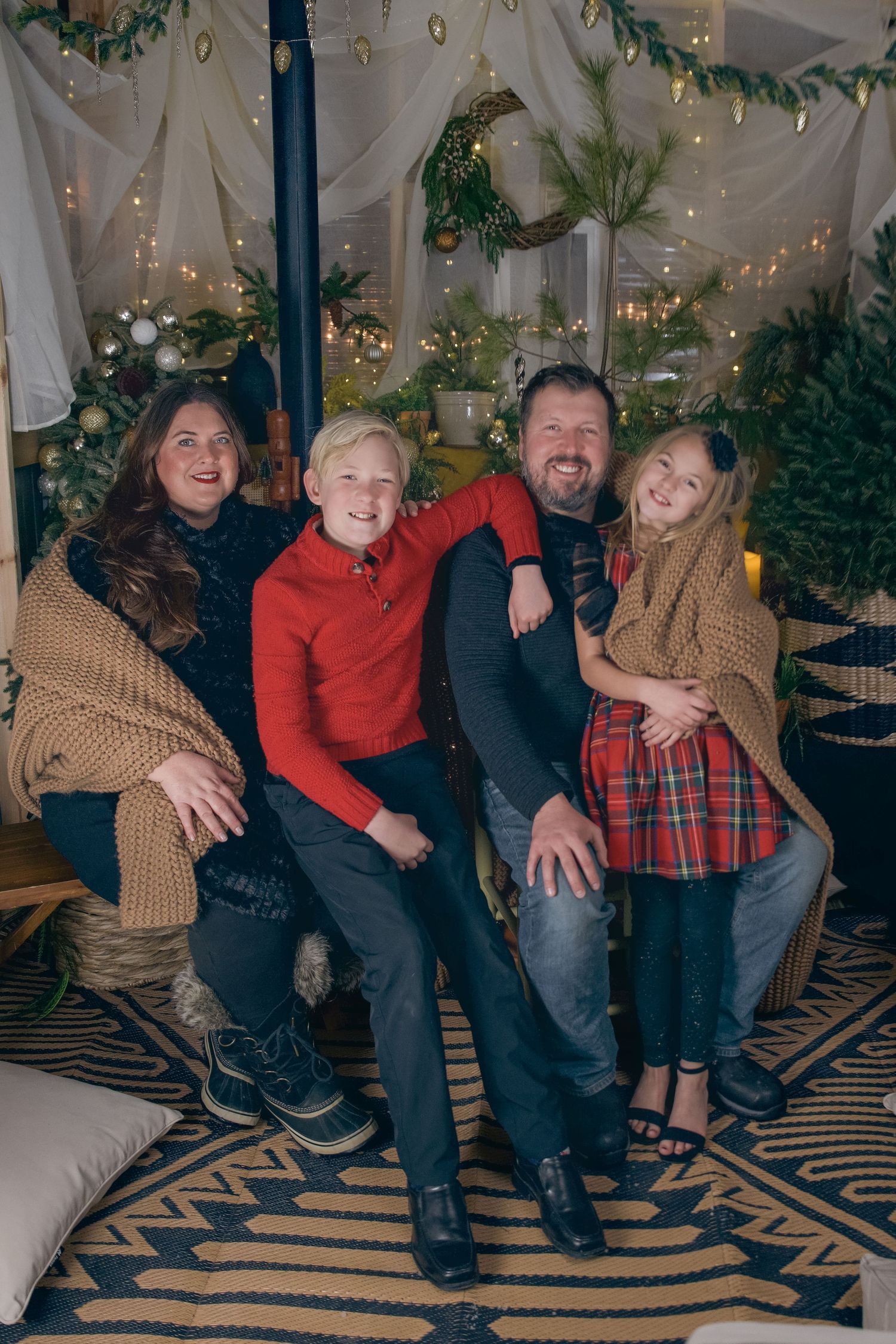 Happy family of four posing together in a festive Christmas decorated room with fairy lights and holiday greenery.
