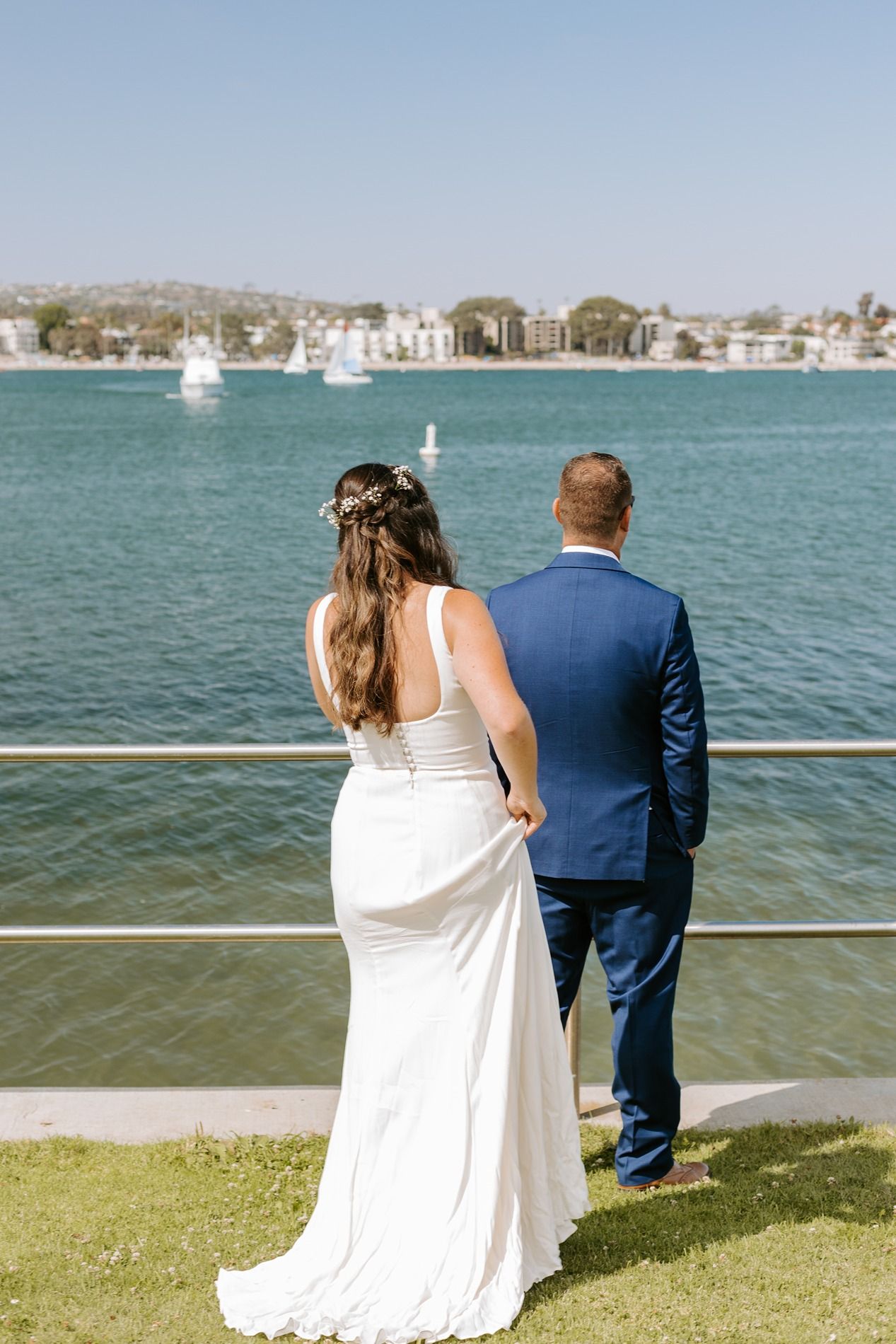 Bride in white gown and groom in blue suit stand hand-in-hand overlooking a scenic waterway on their wedding day at Tower Beach Club.