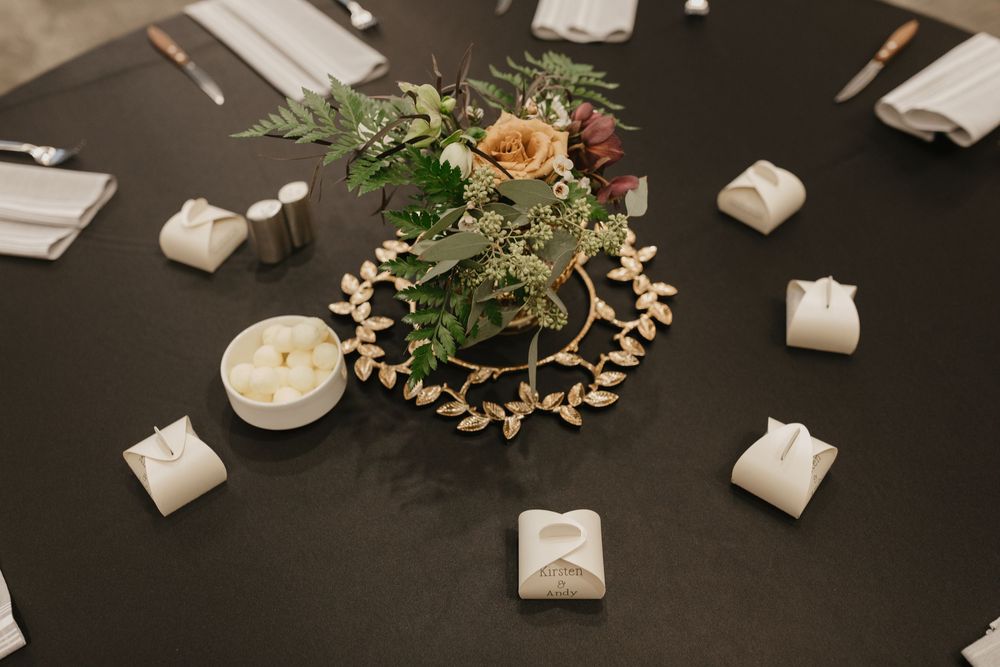 Elegant wedding table centerpiece with flowers, greenery, and small white favor boxes.