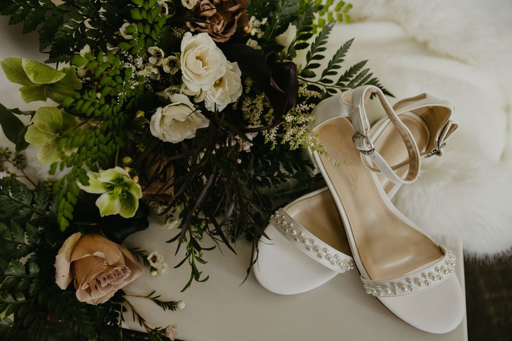 White bridal heels with pearl details beside a lush wedding bouquet of white roses and greenery.
