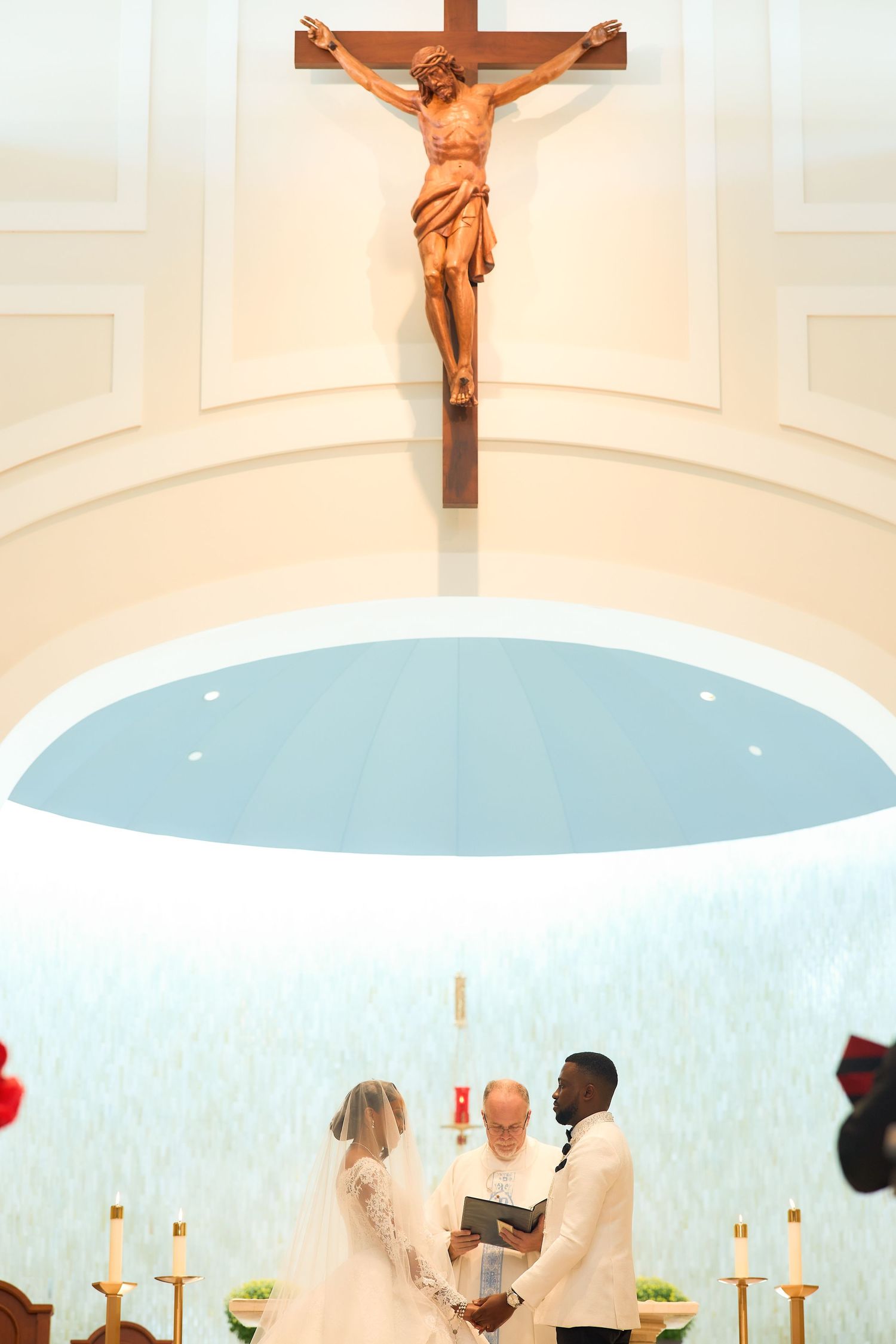 Interracial couple exchanges wedding vows at a Catholic church altar beneath a wooden crucifix.