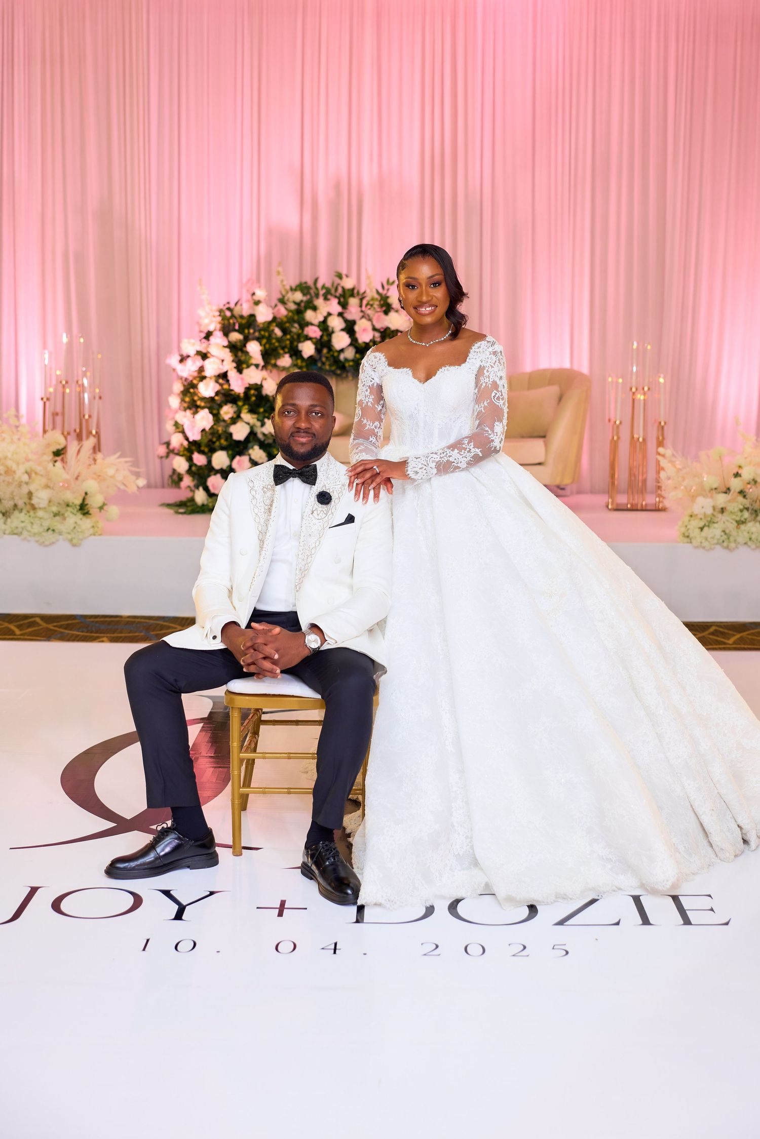 Bride and groom pose elegantly at their wedding reception on 10.04.2023, with floral backdrop and monogrammed dance floor.