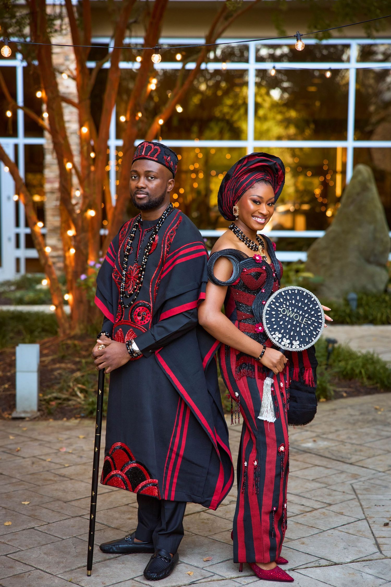 Couple in matching black and red African traditional attire posing outdoors at evening event.