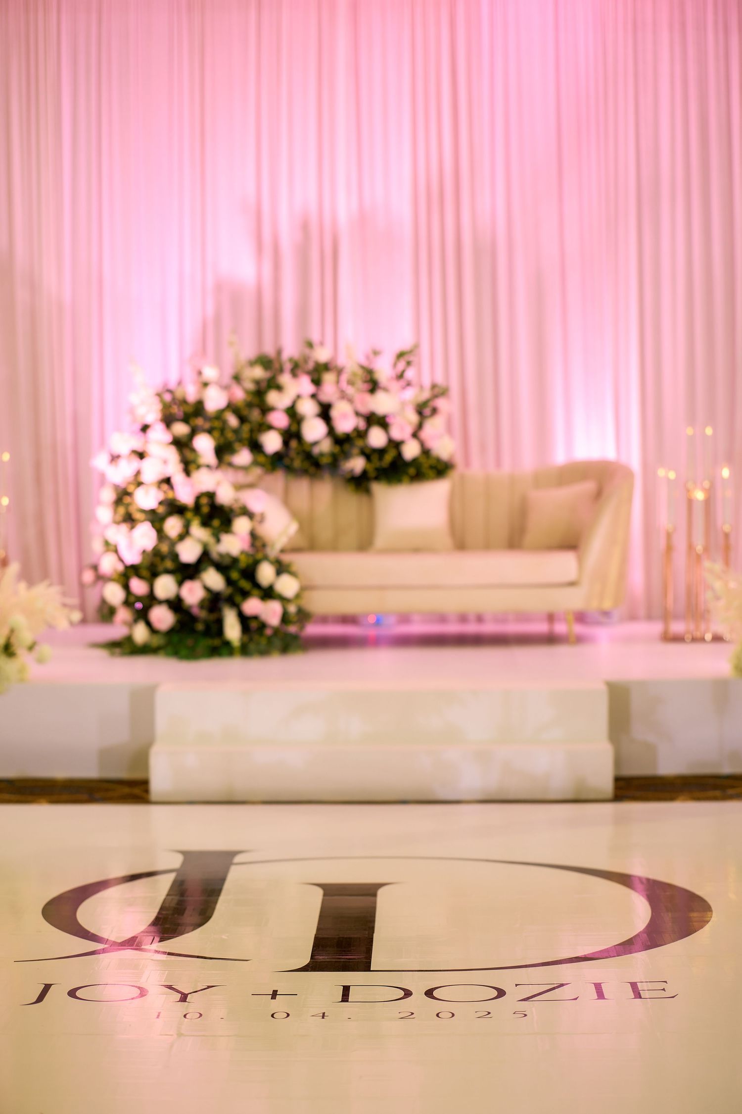 Elegant wedding reception stage with pink draping, floral arrangements, and Joy + Dozie monogram on dance floor.