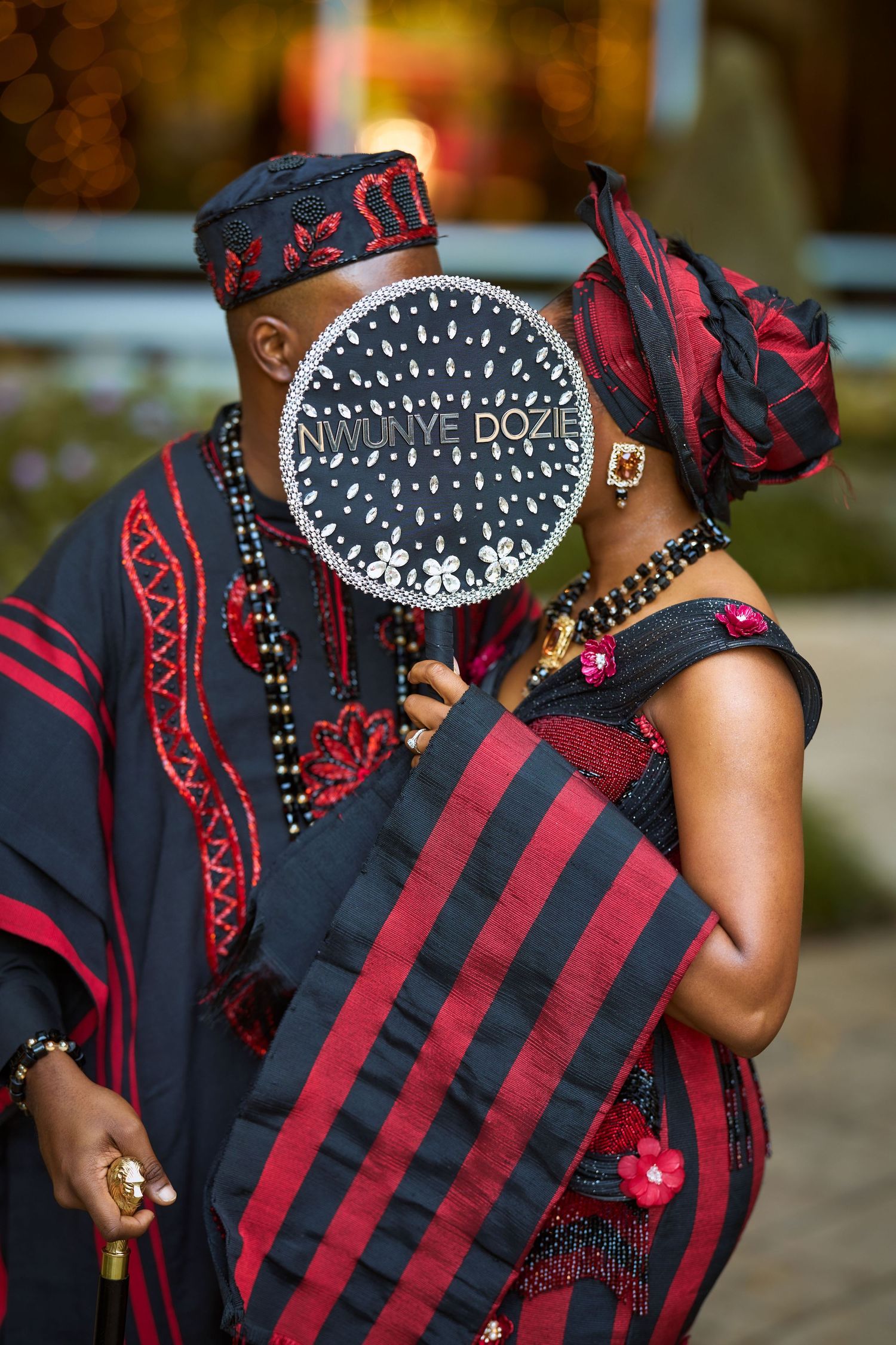 Couple in traditional African attire with black and red garments, beaded accessories, and matching head coverings at a ceremony.