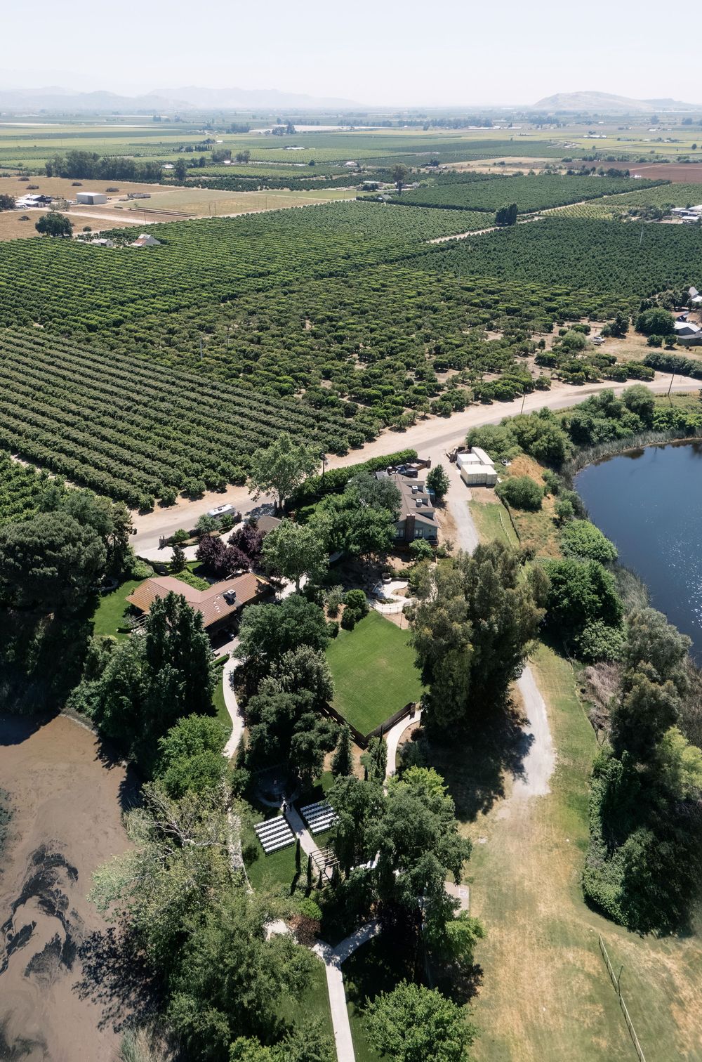 Aerial view of a lush vineyard estate with manicured grounds, pond, and rows of grapevines stretching to distant mountains.
