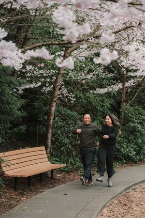 Couple laughing and walking together on a park path under blooming cherry blossom trees in spring.
