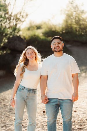 Smiling couple holding hands in jeans and white tops during golden hour outdoor photo session.