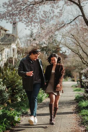 Couple walking hand in hand on a tree-lined path with cherry blossoms in spring.