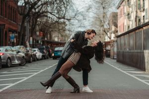 Couple sharing a romantic dip kiss on a city street, surrounded by parked cars and bare trees.