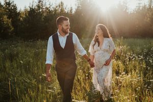 A couple walks hand-in-hand through a sunlit meadow, the golden backlight creating a romantic glow around them.