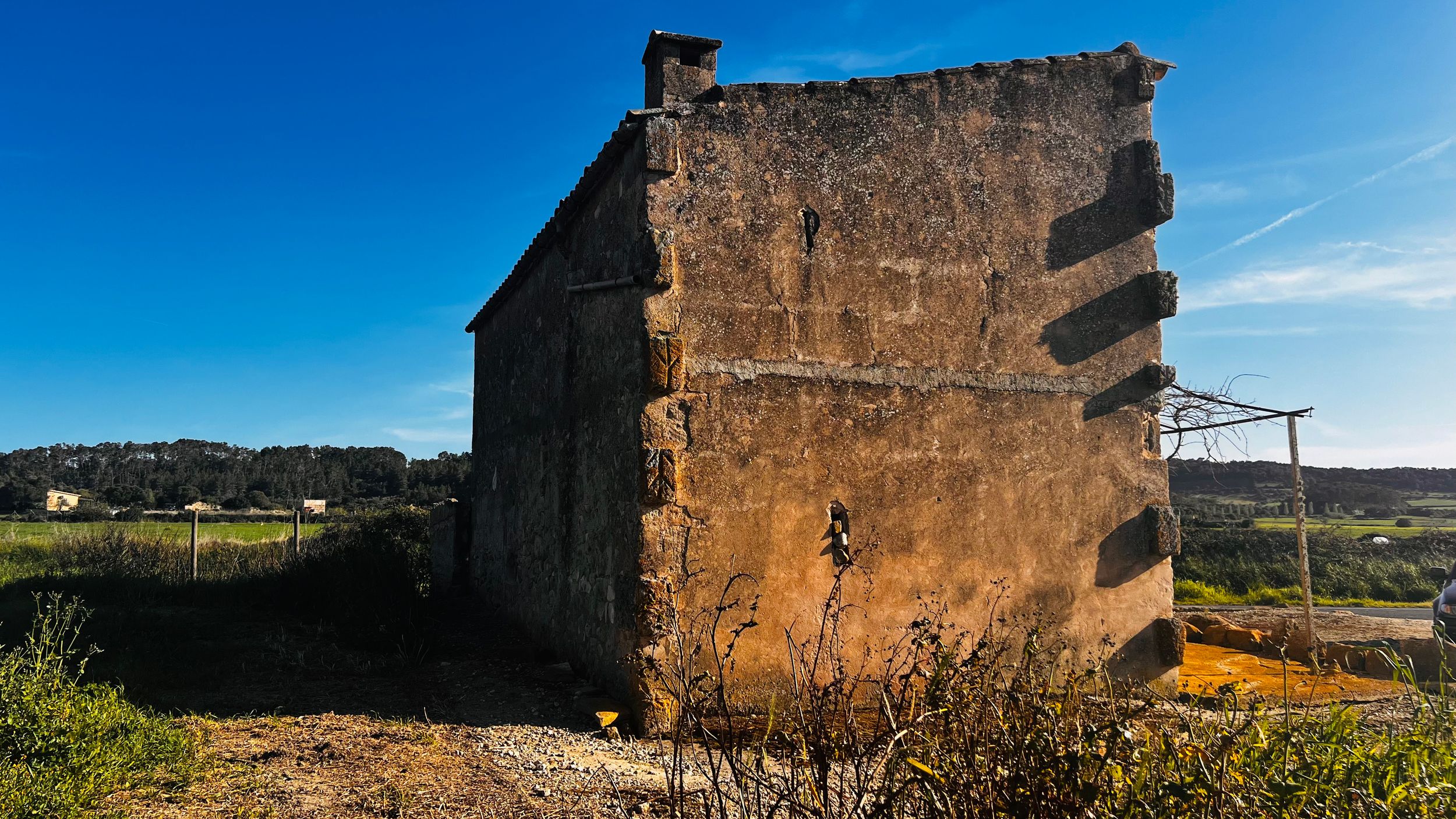 Abandoned stone building with weathered walls under a clear blue sky in a rural Mediterranean landscape.