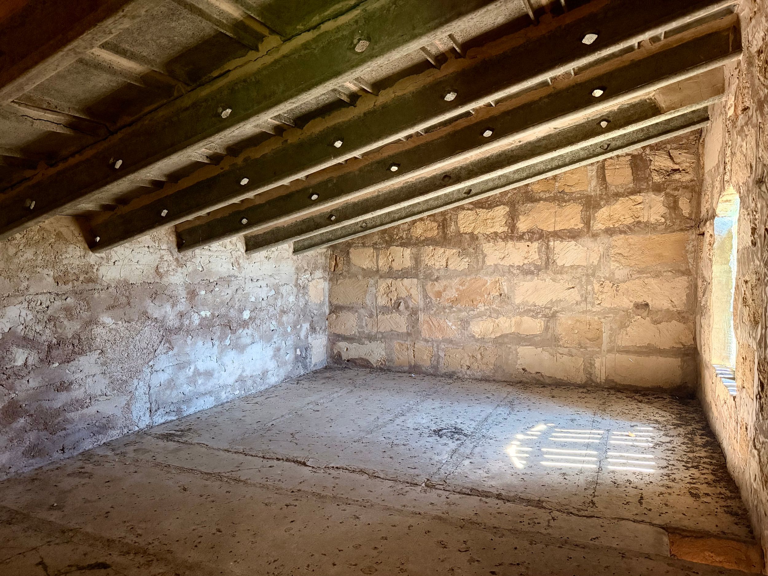 Rustic stone basement room with exposed wooden beam ceiling, recessed lighting, and rough concrete floor.
