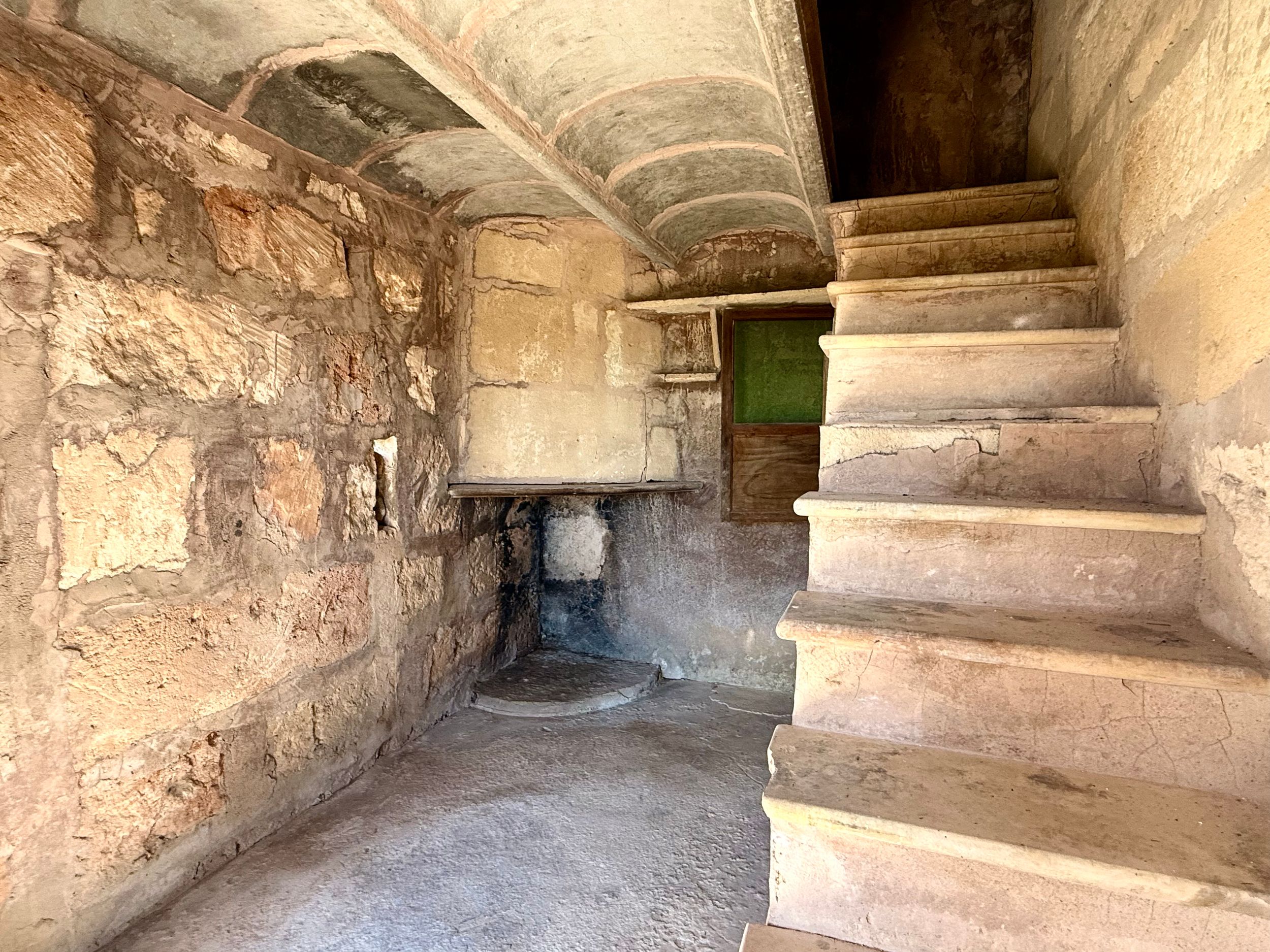 Ancient stone staircase and arched interior of a historic structure with weathered walls and a green doorway.