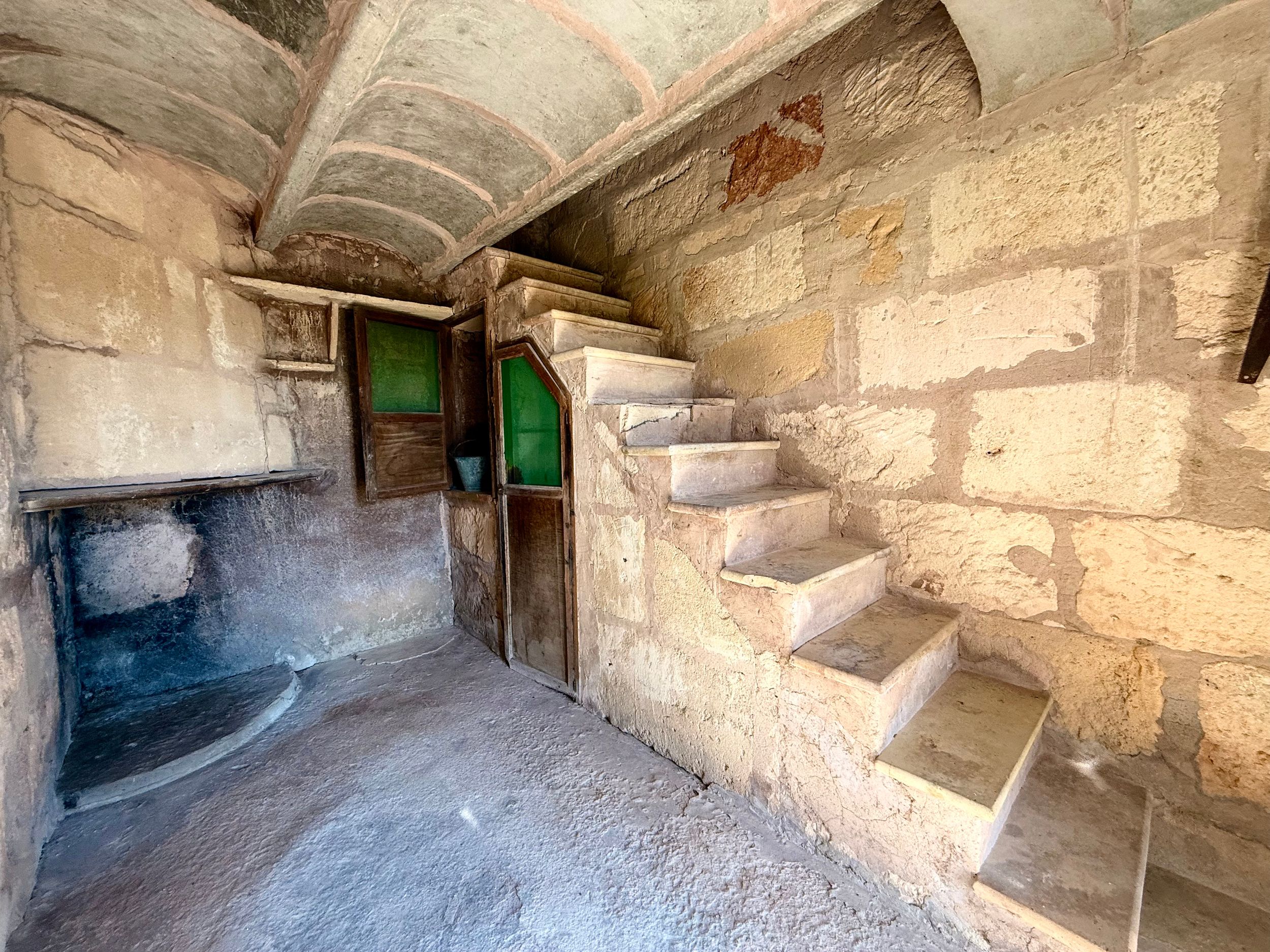 Ancient stone staircase inside a historic building with arched ceiling, wooden door, and rustic stone walls.