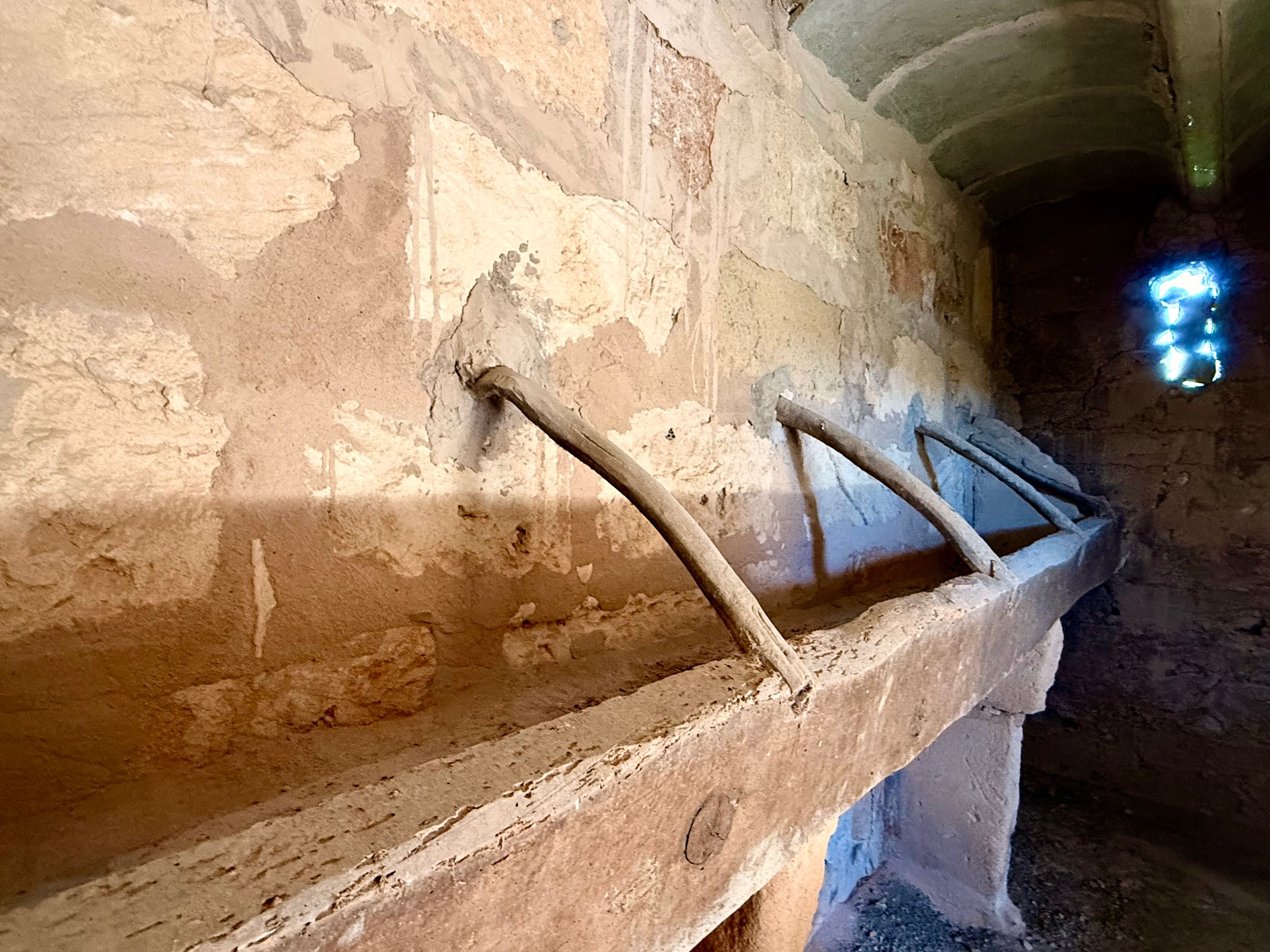 Ancient stone trough with metal brackets mounted on weathered wall inside historic vaulted stone structure.