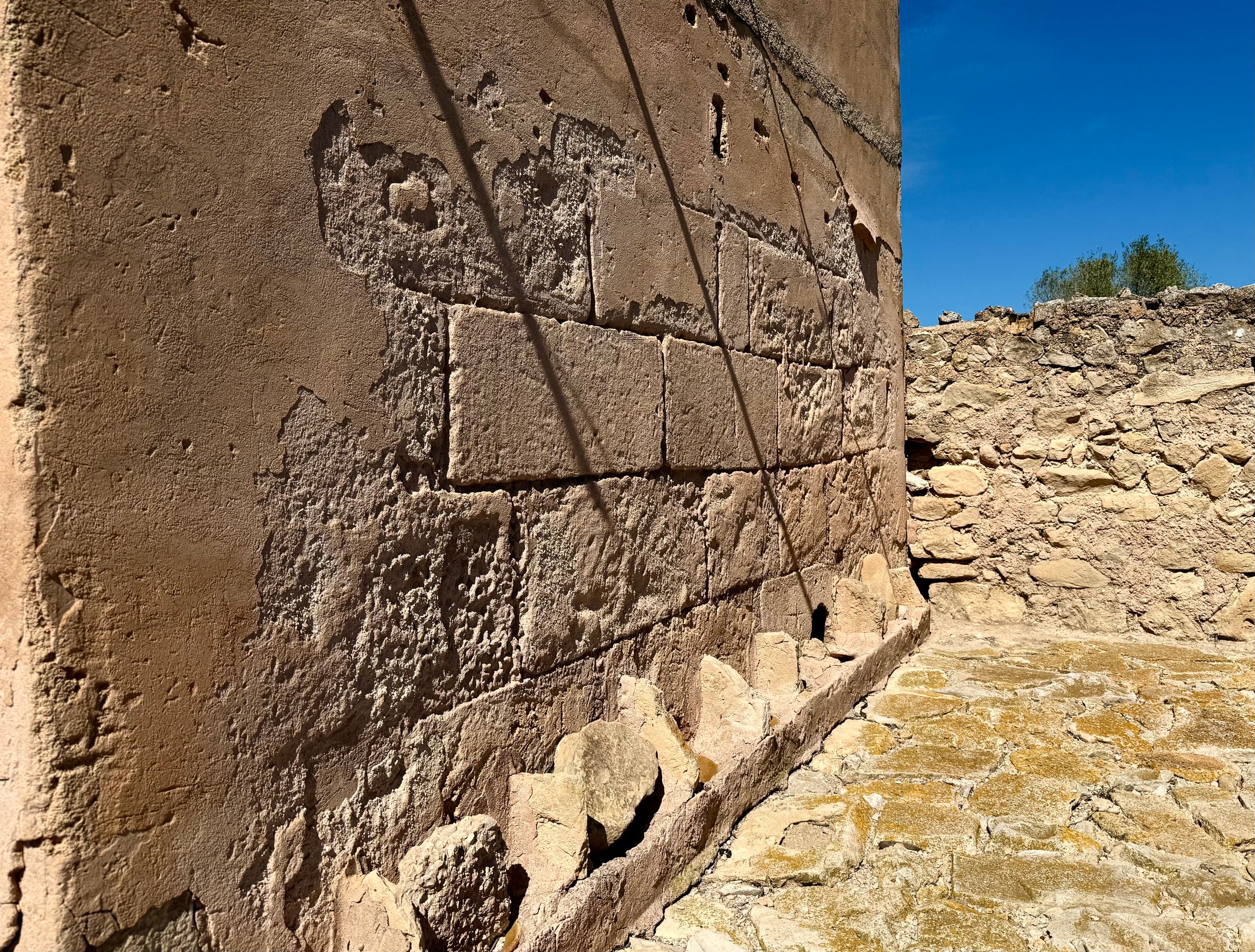 Ancient stone wall with carved geometric patterns at an archaeological site under a clear blue sky.