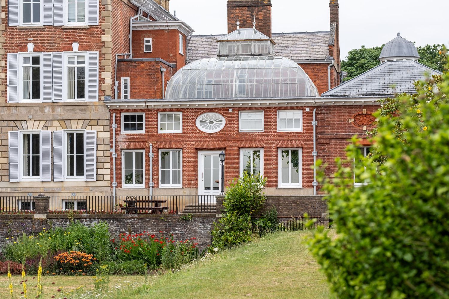 Historic brick building with distinctive domed glass conservatory surrounded by landscaped gardens and residential architecture.
