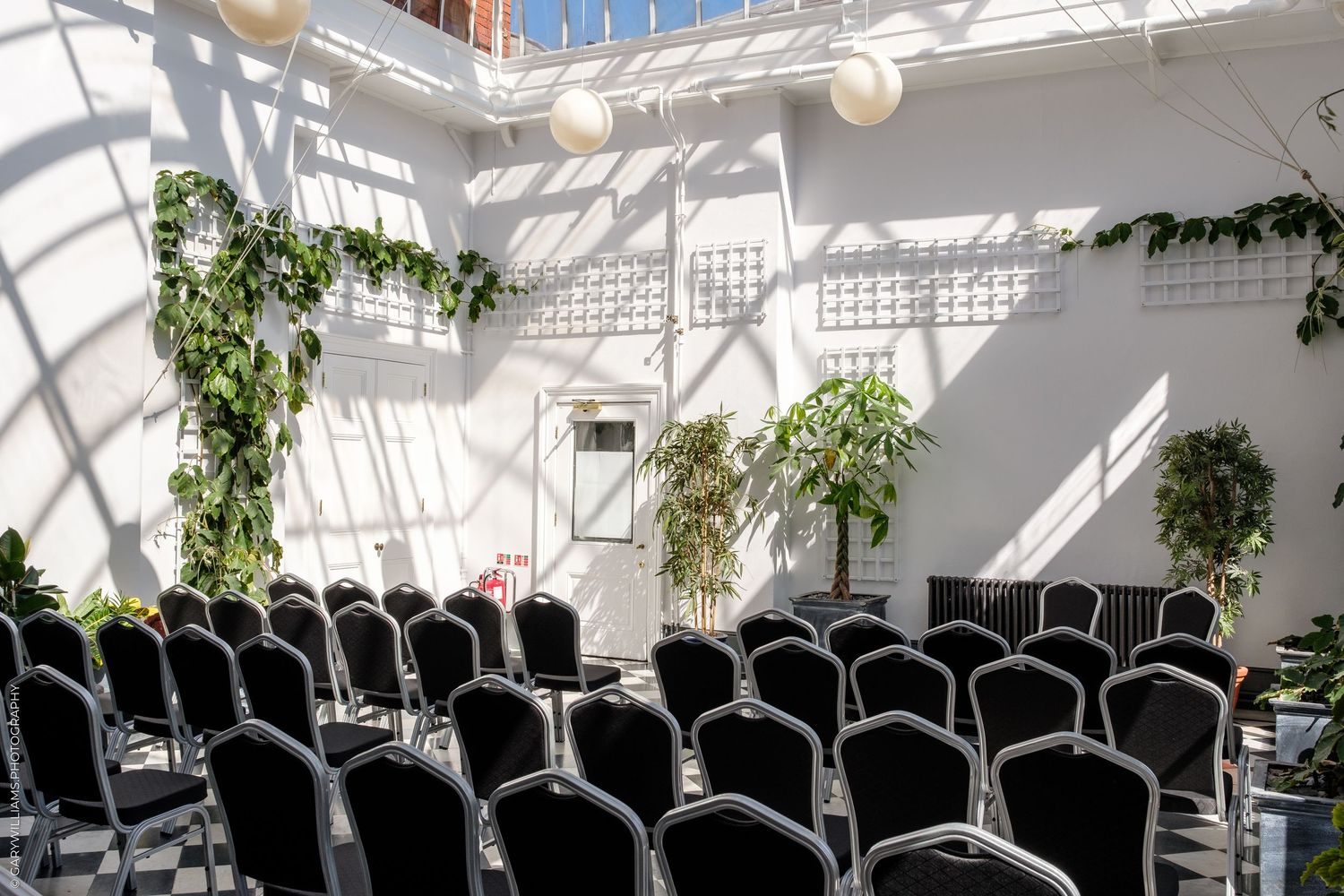 Elegant indoor ceremony space with rows of black chairs, white walls, green plants, and natural light from skylights.