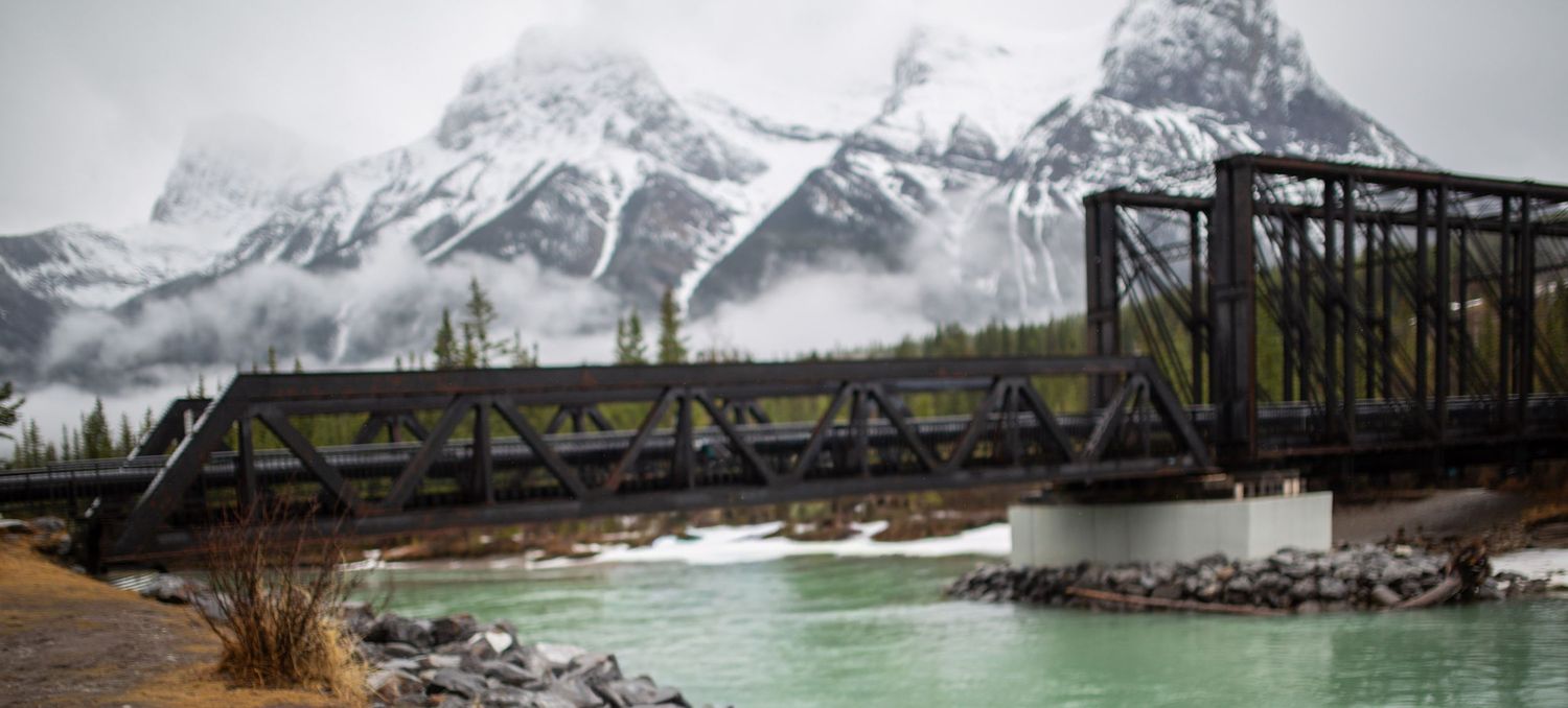 Railway bridge over the Bow River in Canmore with the Rocky Mountains behind, photographed by RezinMedia