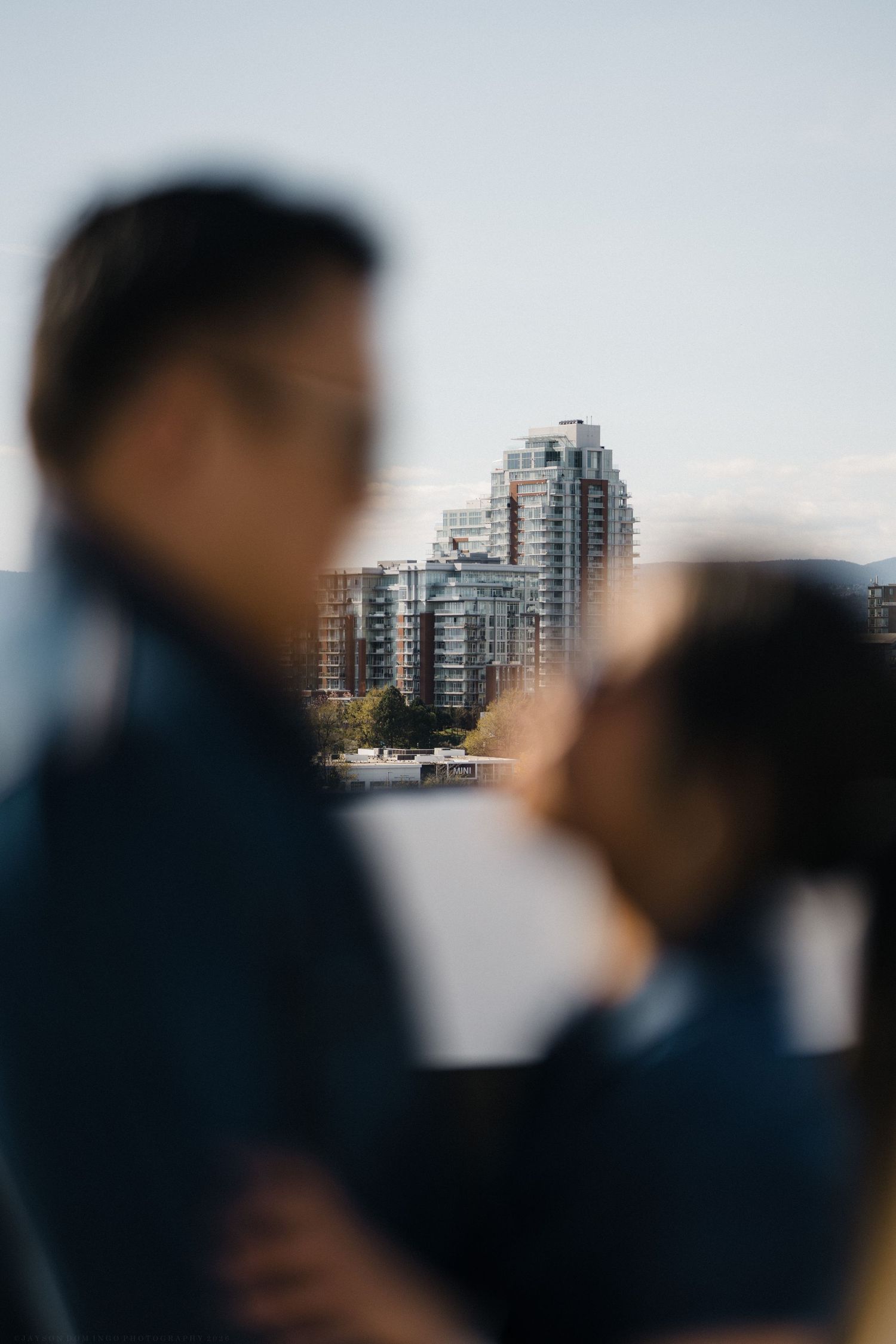 Couple sharing a tender kiss with blurred city buildings in the background.