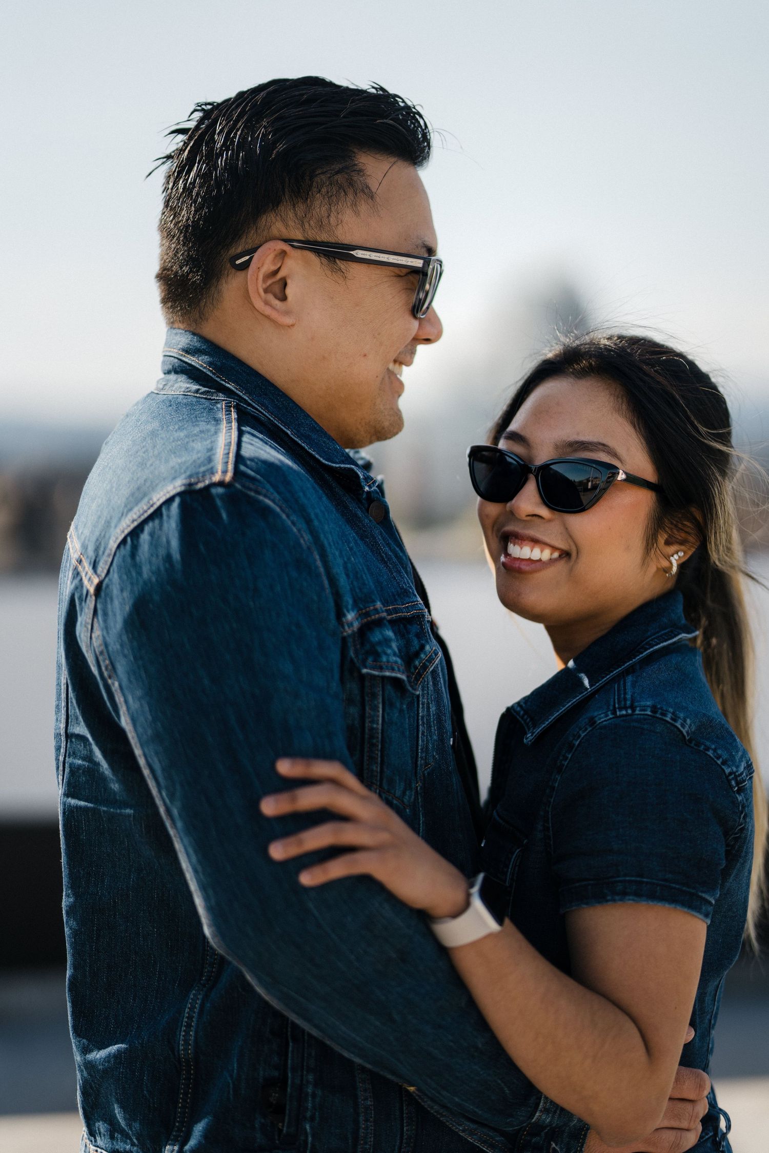 Happy couple in denim outfits embracing and smiling at each other on a rooftop on a sunny day.