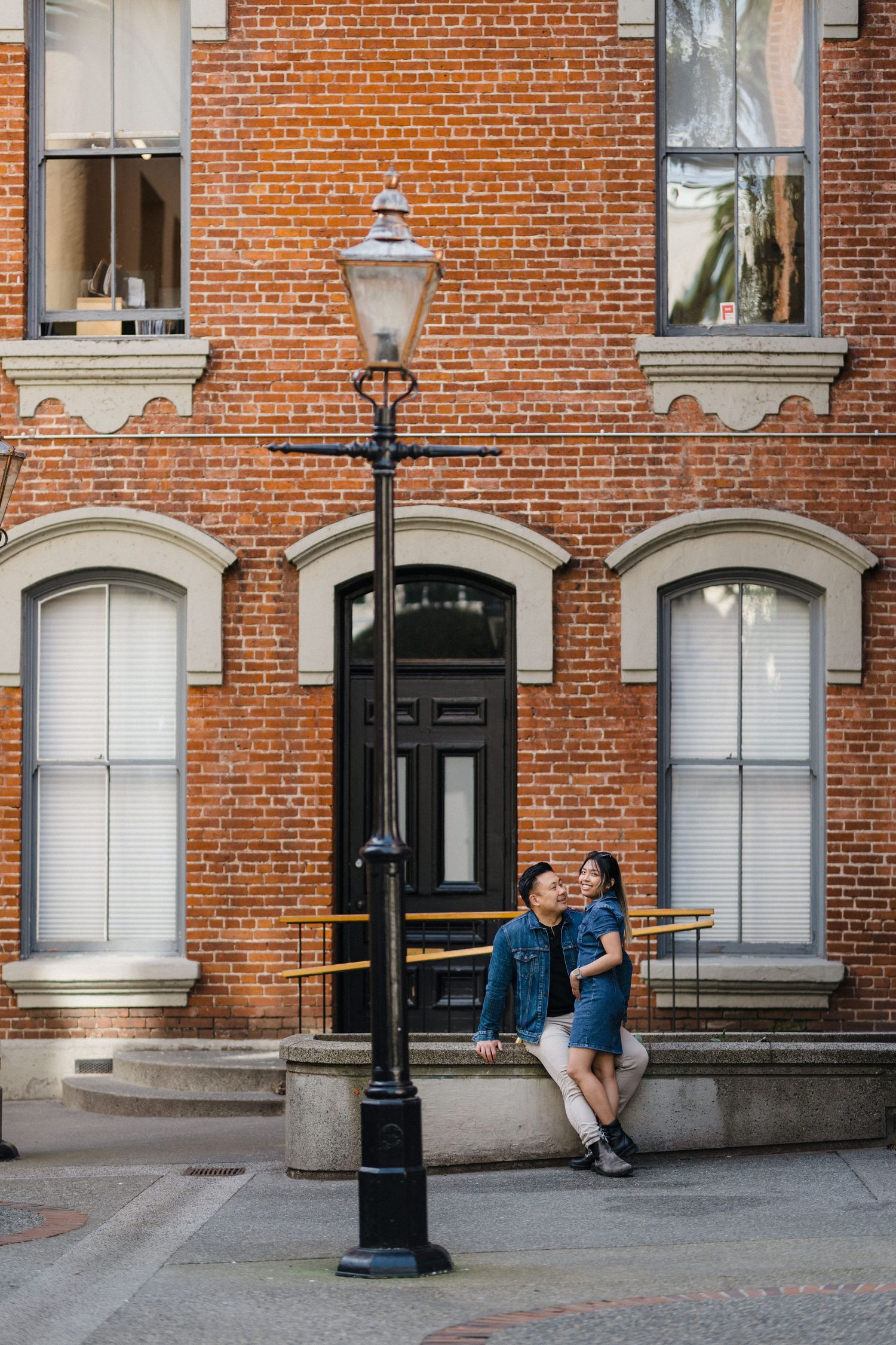 Couple embracing by a vintage lamp post against a classic red brick building.