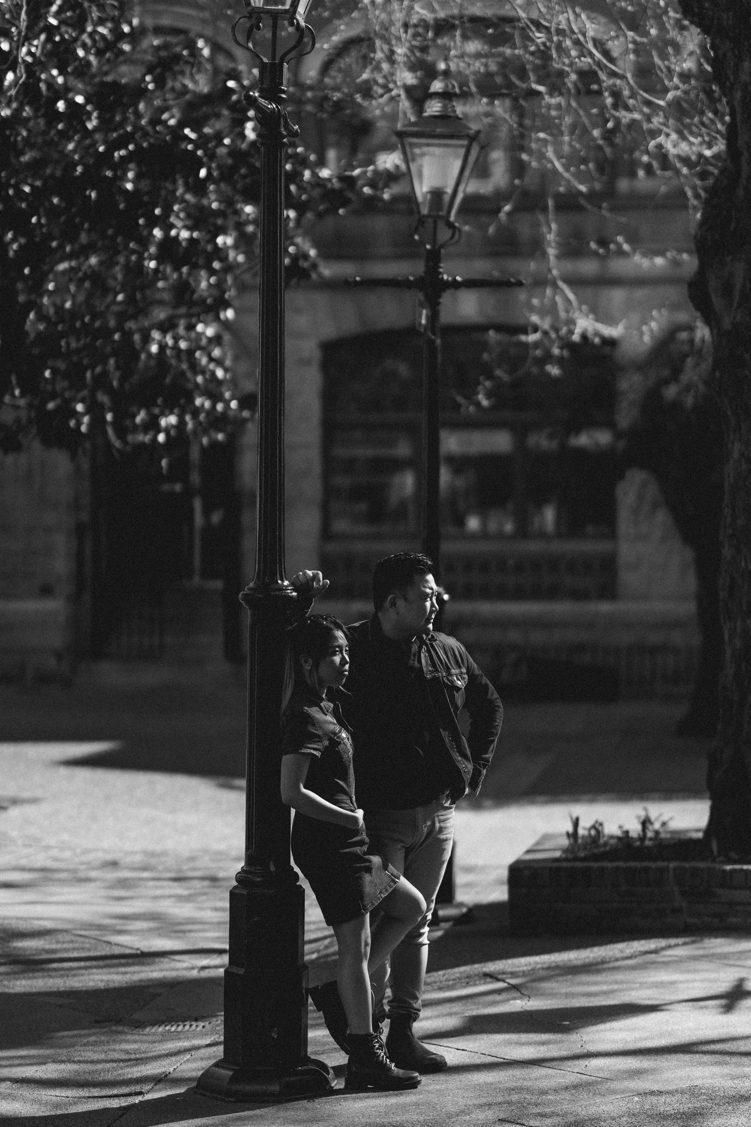Black and white photo of a romantic couple leaning against a vintage street lamp in an urban setting.