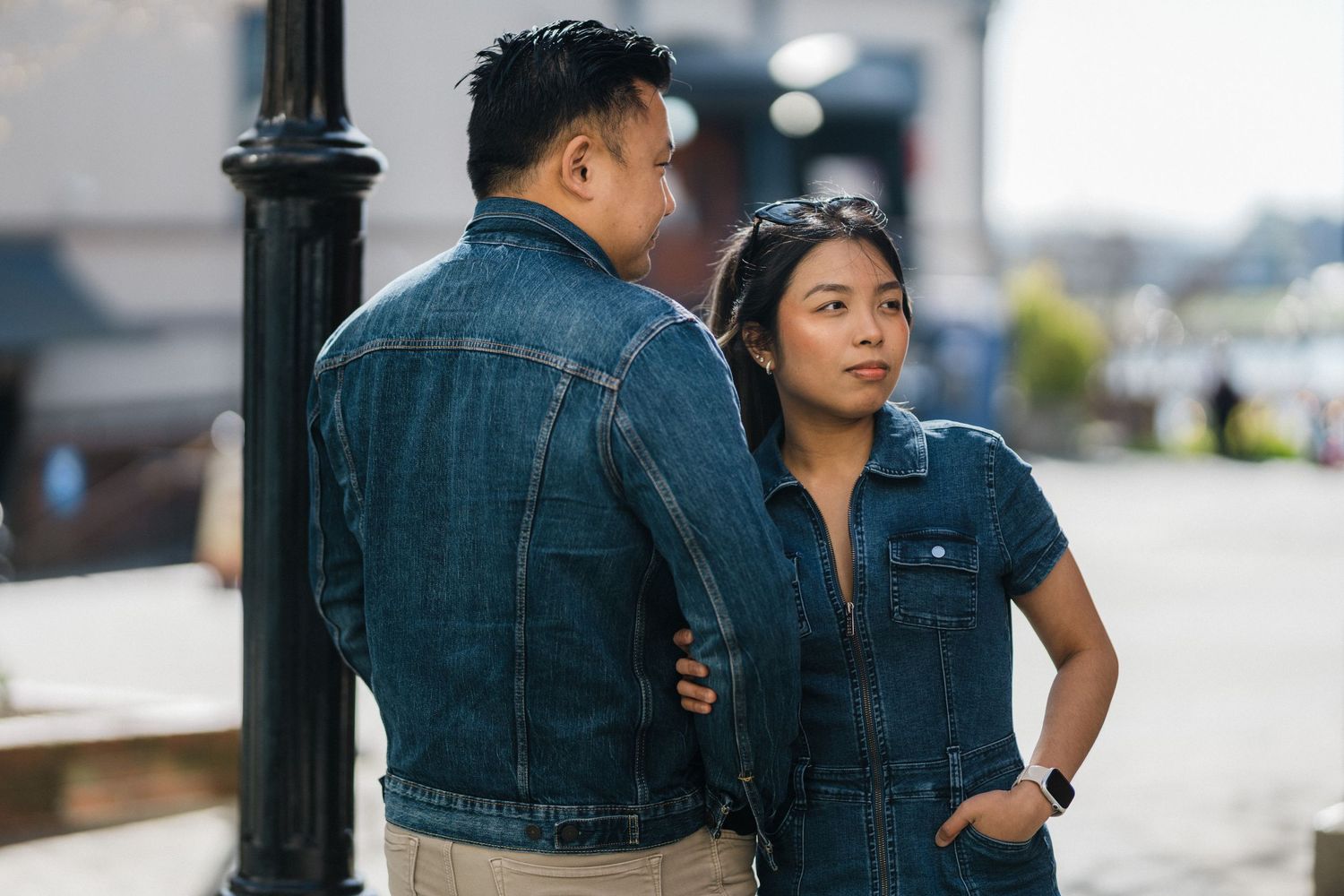 Asian couple in matching denim outfits standing by a lamppost, woman looking back over her shoulder.