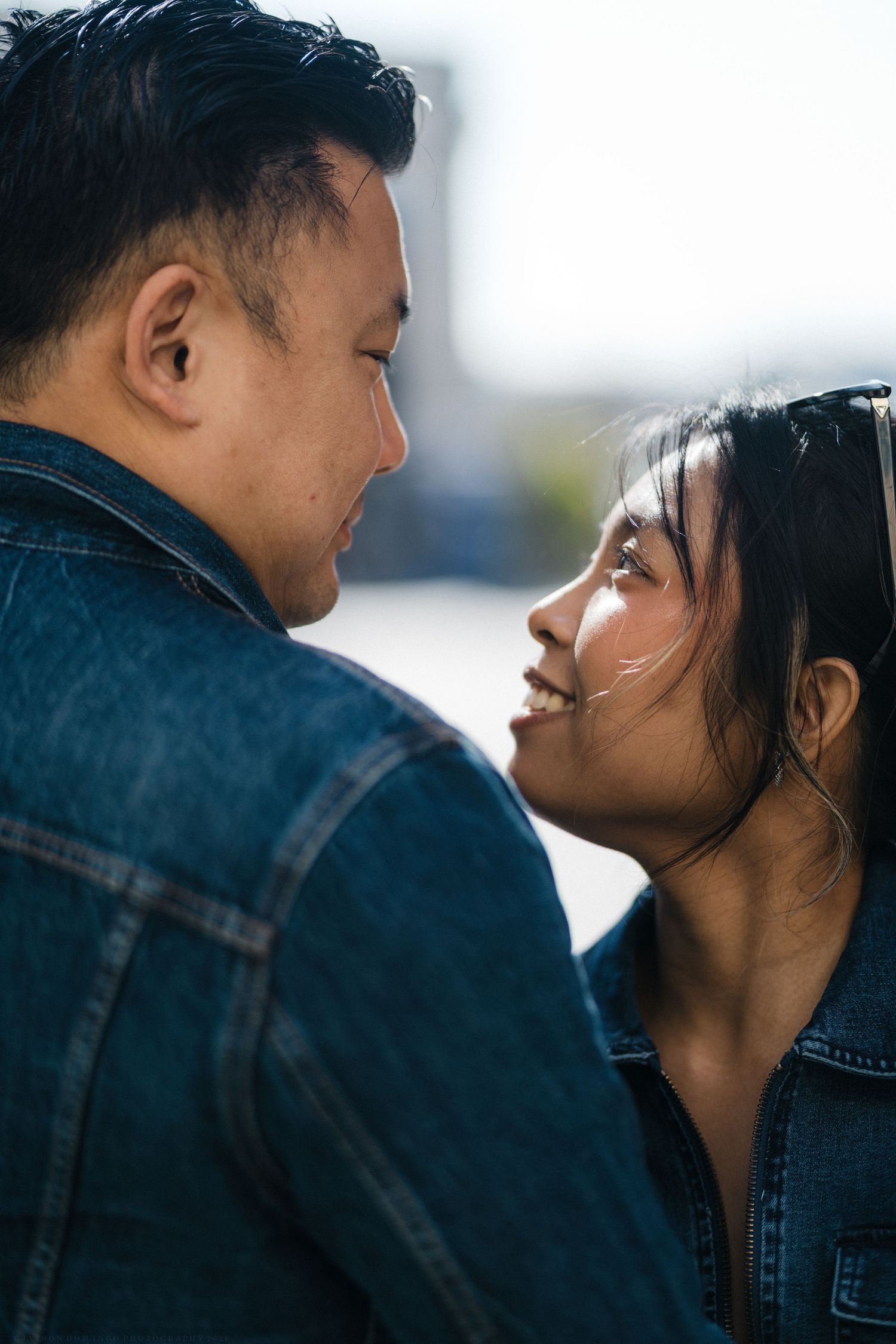 Close-up of a couple nearly kissing, the woman smiling up at the man in matching denim jackets outdoors.