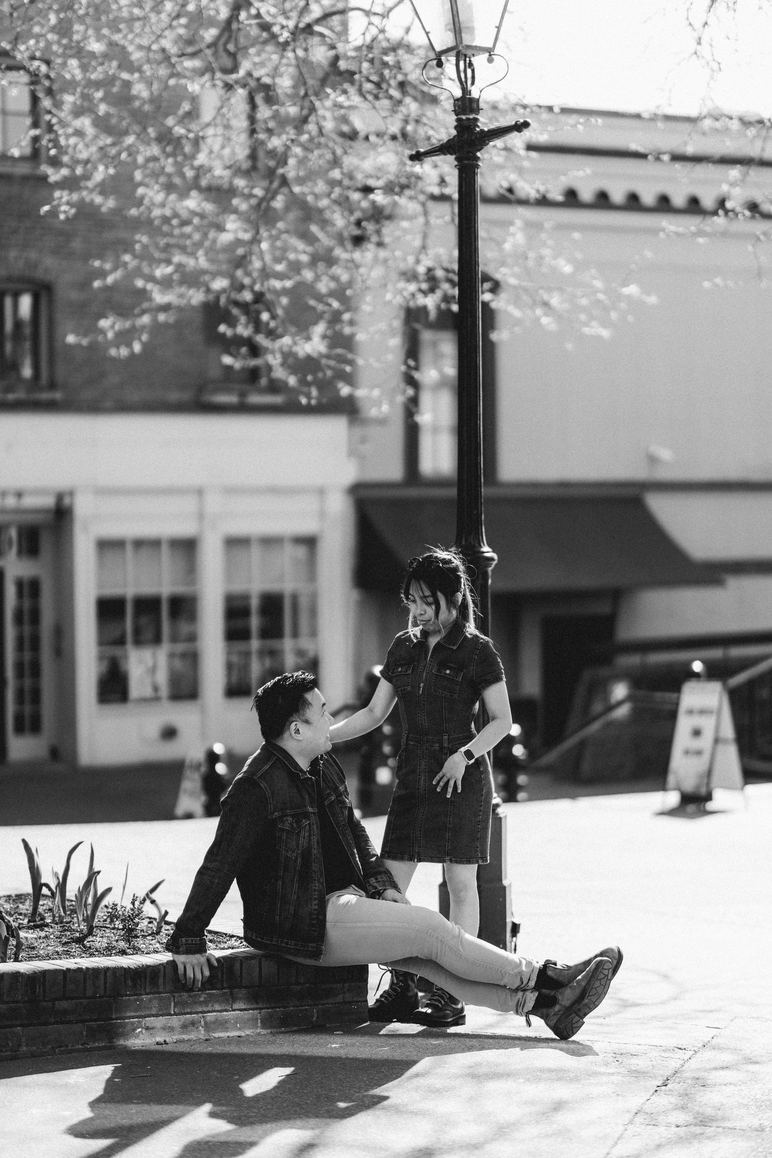 Black and white photo of Asian couple relaxing by lamppost in sunny urban plaza.